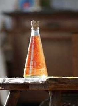 Eine durchsichtige Glasflasche mit Korkverschluss, gefüllt mit orangefarbenem Öl. Die Flasche steht auf einem rustikalen Holztisch in einem Raum mit unscharfem Hintergrund.