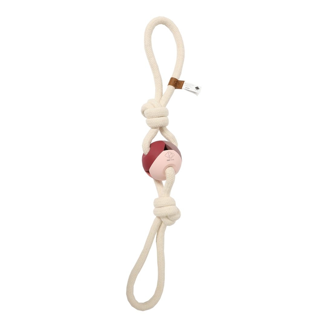 Cremefarbenes Hundespielzeug aus Seil mit zwei Knoten und einer rot-rosa Kugel in der Mitte; strukturierte Oberfläche, kleines Etikett am oberen Knoten.