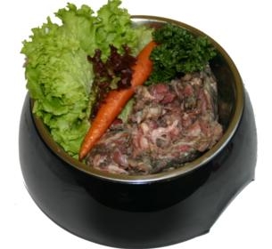 Eine schwarze Futterschale mit rohem, grob gewolftem Fleisch. Dekoriert mit frischem grünem Salat, roter Blattsalate, einer Karotte und einem Zweig Petersilie.