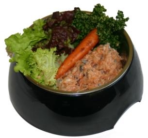 Ein schwarner Napf mit gewolftem Lachs in rosa-orange Farbe, durchsetzt mit dunklen Stückchen. Daneben liegen ein ganzer Karotte sowie grüne und rote Salatblätter.