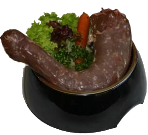 Rohes Putenhalsstück in schwarzer Schale, umgeben von grünem Blattgemüse und einem Stück orangefarbener Karotte auf hellem Hintergrund.