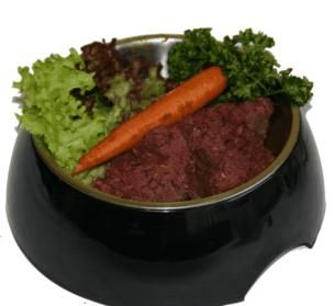Ein Napf mit gewolftem Kaninchenmix in dunklem Rotbraun, daneben eine Möhre und verschiedene Salate, Gesamtbild wirkt frisch und naturbelassen.