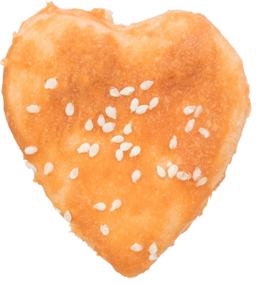 Ein getrockneter Kauartikel für Hunde in Herzform, goldbraun gefärbt. Die Oberfläche wirkt leicht glänzend und unregelmäßig, mit fester, zäher Struktur und einzelnen hellen Saatkörnern.