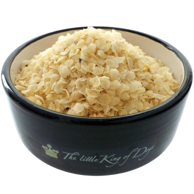 Reisflocken Ein schwarzer Napf mit der Aufschrift „The little King of Dogs“, gefüllt mit blassgelben, dünnen Flocken mit leicht unregelmäßiger, splitterartiger Struktur.Barfen