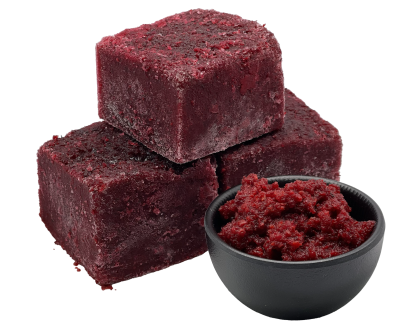 Drei gefrorene, dunkelrot-violette Würfel aus püriertem Gemüse. Daneben steht eine schwarze Schale mit aufgetauter, grobkörniger Gemüsemasse in kräftigem Rot.