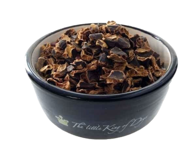 Grob gebrochene Stücke von dunkelbraunem Johannisbrot, unregelmäßig geformt, aufgeschichtet in einer dunkelblauen, runden Schale mit hellem Innenrand.