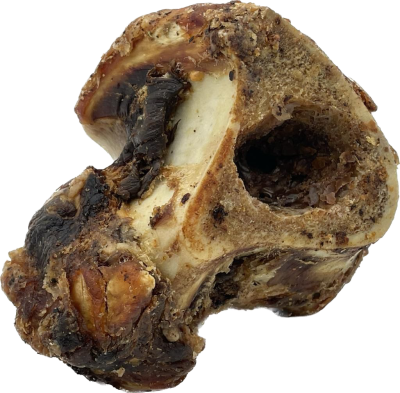 Ein grob strukturierter, unregelmäßig geformter Rindergelenkknochen mit dunklen, getrockneten Fleischresten und einer sichtbaren Knochenöffnung im oberen Bereich.