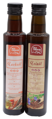 Zwei braune Glasflaschen mit schwarzem Schraubverschluss und Etiketten der Marke „Wild Canadian“. Links steht „Lachsöl“ mit Fischabbildung, rechts „Leinöl“ mit Leinsamen und Blüten.