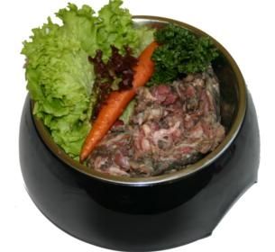 Eine schwarze Futterschale mit rohem, grob gewolftem Fleisch. Dekoriert mit frischem grünem Salat, roter Blattsalate, einer Karotte und einem Zweig Petersilie.