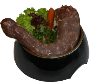 Rohes Putenhalsstück in schwarzer Schale, umgeben von grünem Blattgemüse und einem Stück orangefarbener Karotte auf hellem Hintergrund.