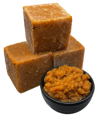Drei gefrorene, orangebraune Würfel aus püriertem Gemüse. Daneben steht eine schwarze Schale mit aufgetauter, stückiger Gemüsemasse in kräftigem Orange.