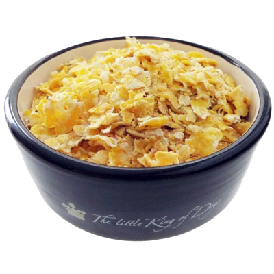 Ein Napf mit gelblich-beigen Getreideflocken mit unregelmäßiger, brüchiger Struktur. Die Flocken sind schichtweise eingefüllt.